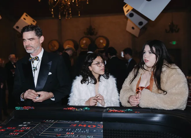 Guests at a Spark craps table under hanging dice at a black-tie gala